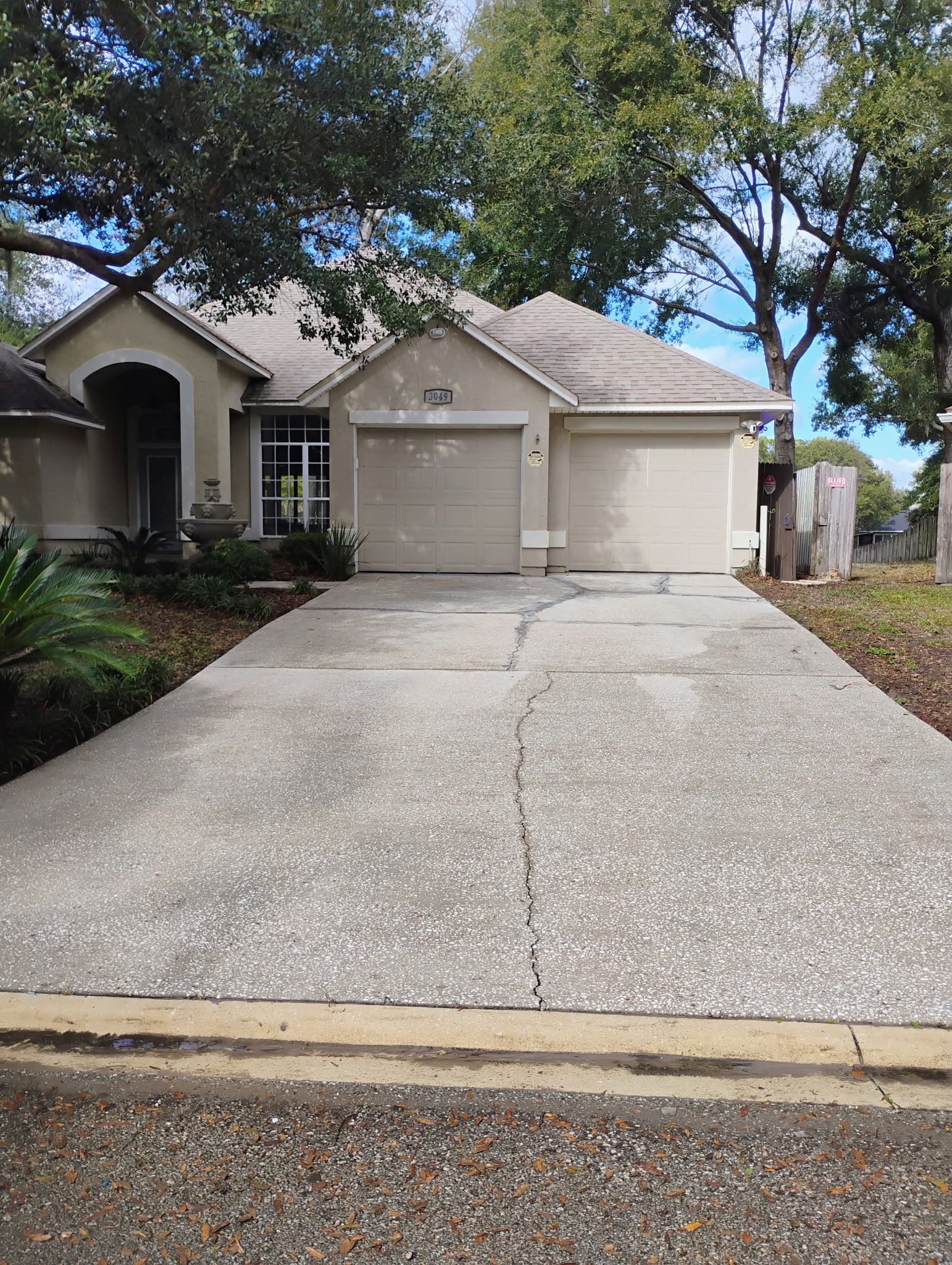 Tan house with concrete driveway, two-car garage, and trees in the background.