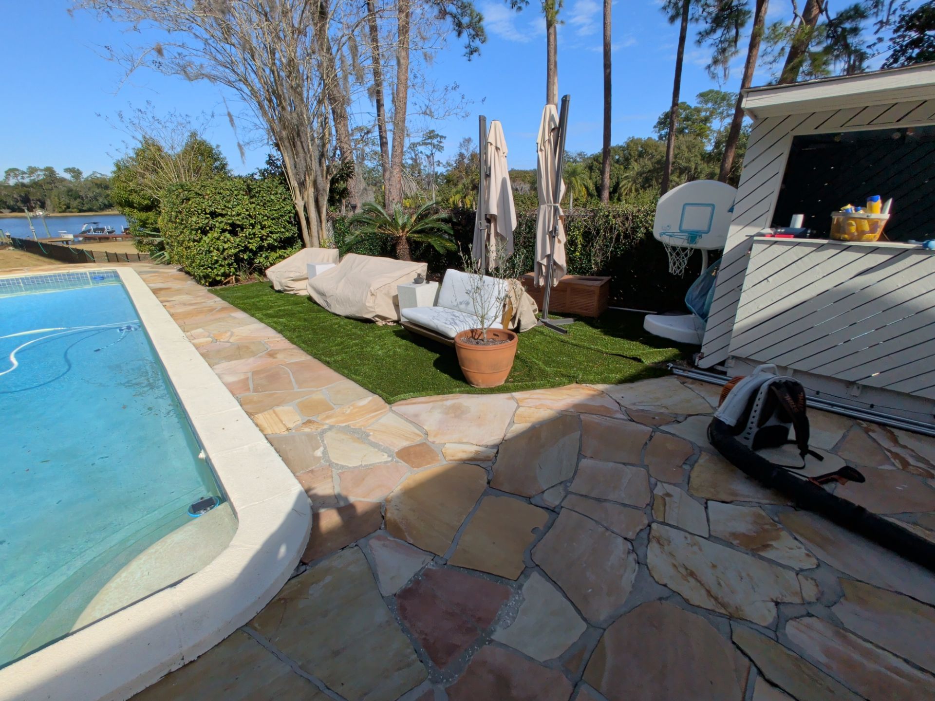 Backyard with pool, patio, seating, and trees on a sunny day.