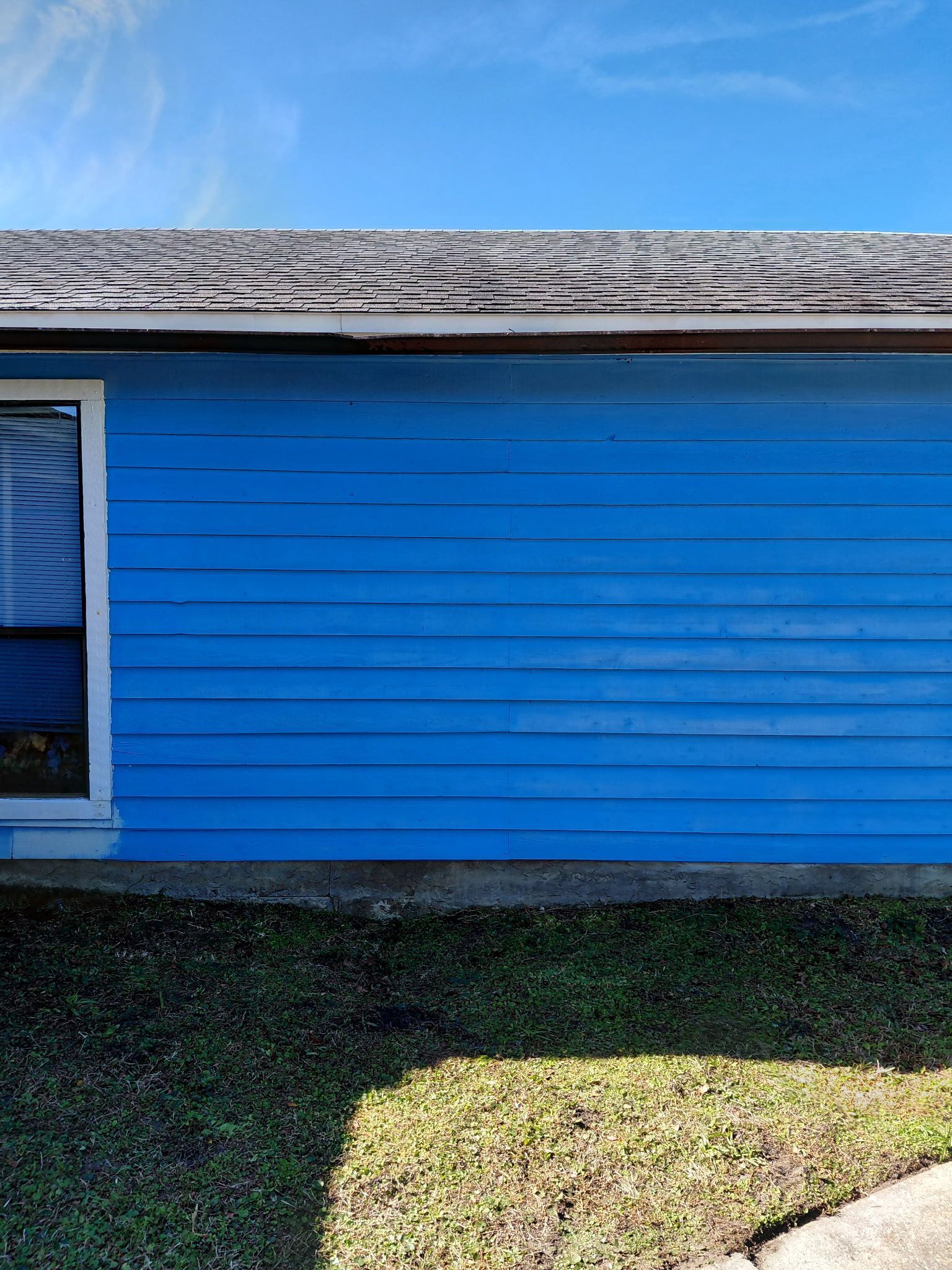 Blue house with window, gray roof, and green grass against a clear blue sky.
