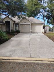 Tan house with two-car garage and long concrete driveway. Large trees frame the house.