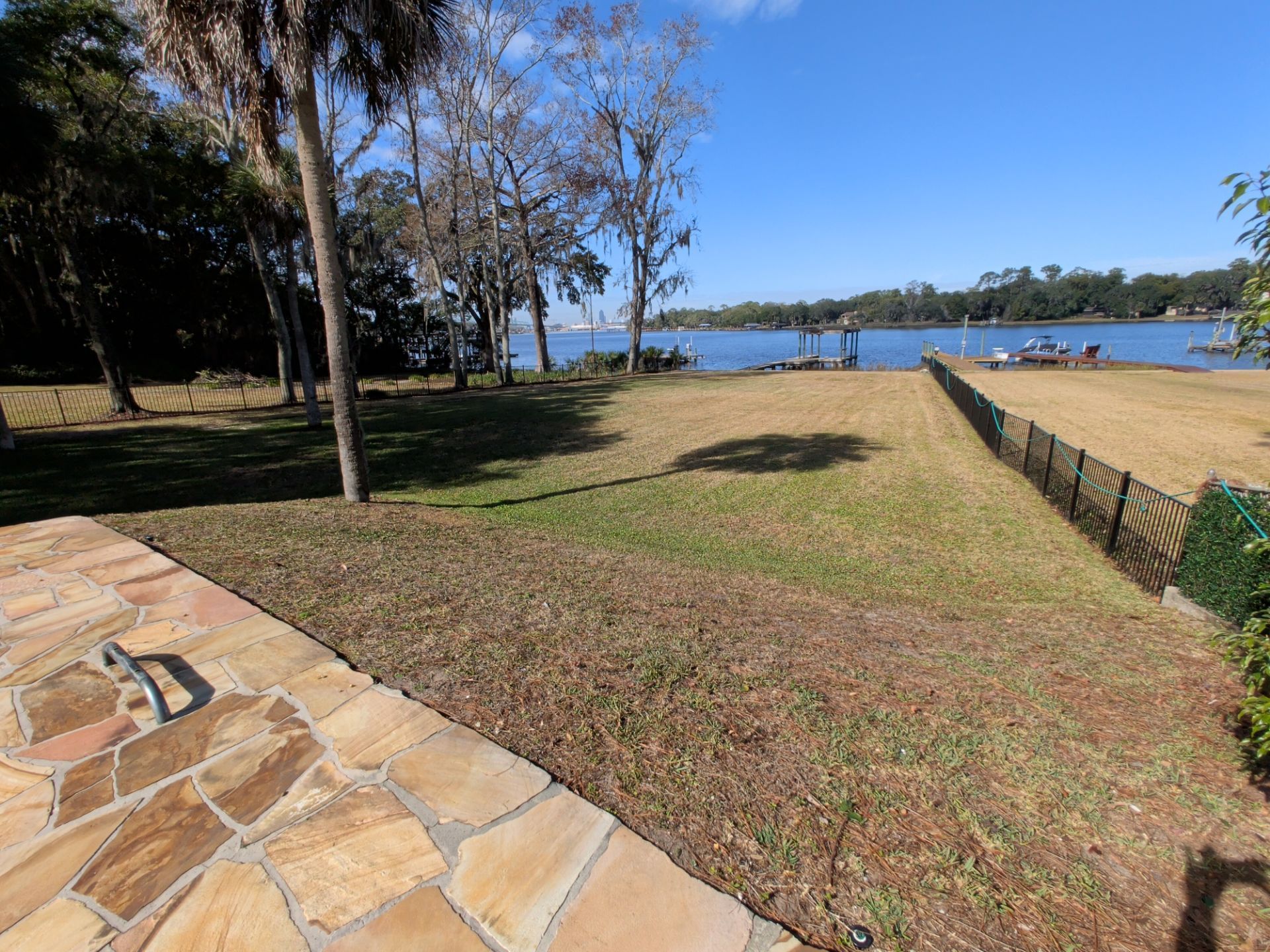 Grassy yard leads to a waterfront with dock and trees under a blue sky.