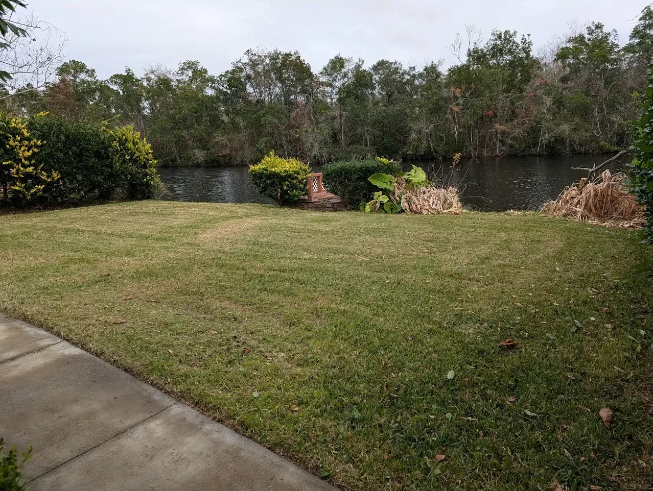 Lawn next to a water canal with trees in the background under a cloudy sky.