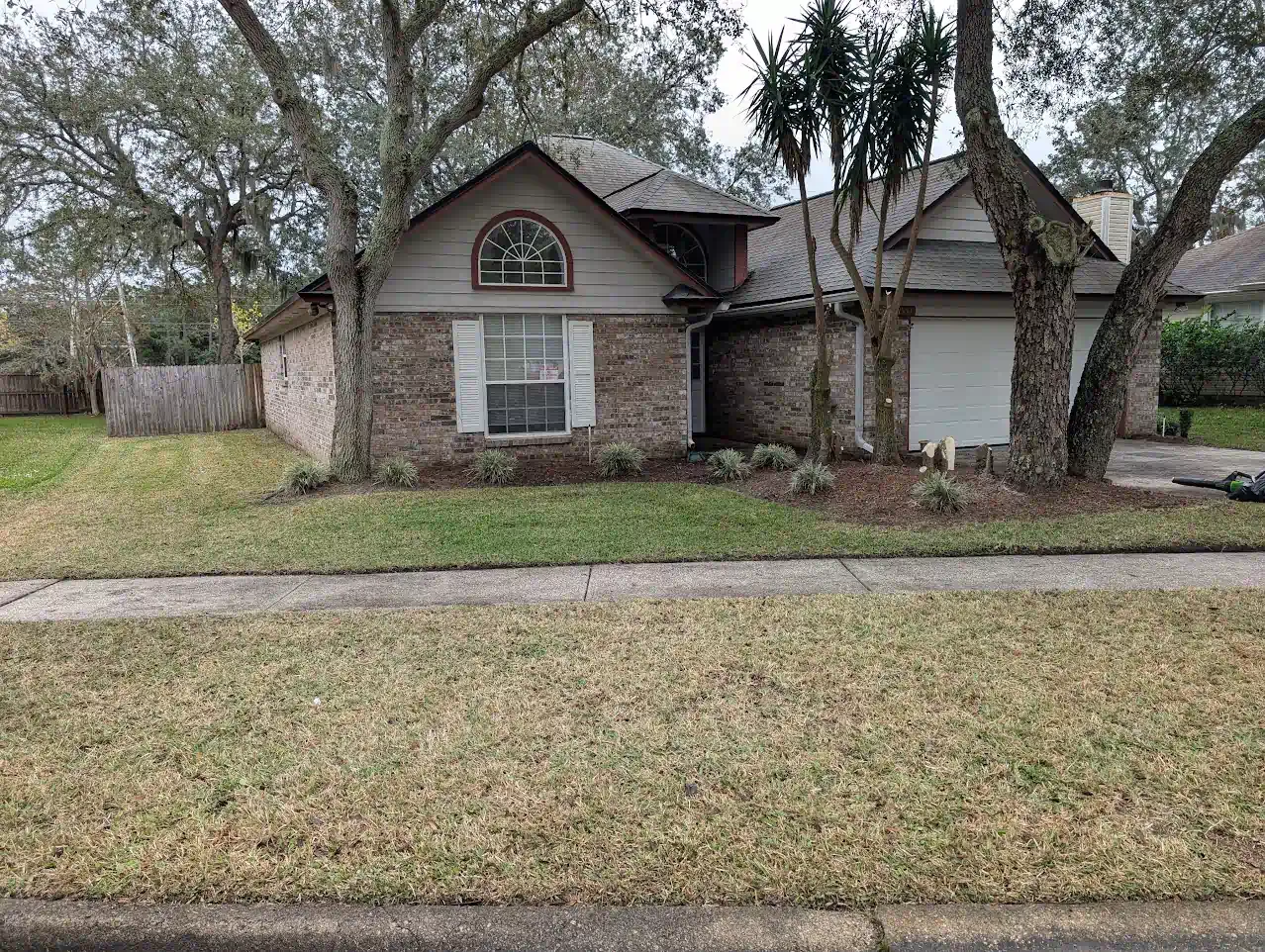 Brick house with brown roof, large trees, and a grassy lawn.
