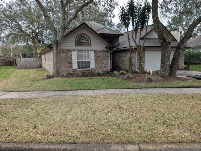 Brick house with a small lawn. Trees frame the house on the sides. Overcast day.