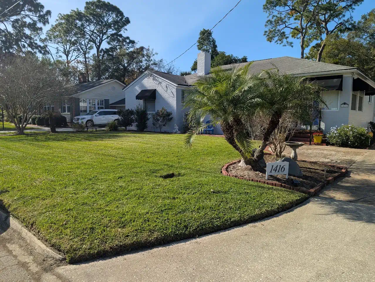 A light blue house with a well-kept lawn, palm tree, and address sign; sunny day.