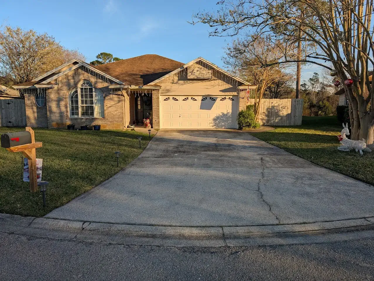 A one-story house with a driveway. The house has a garage, window, and a mailbox. A tree is on the right.