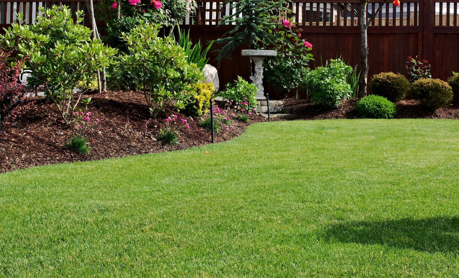 Landscaped garden with green lawn, shrubs, flowers, and a wooden fence