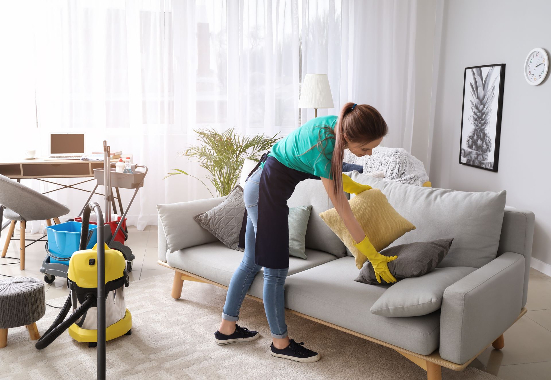 Person cleaning a gray upholstered chair with a vacuum attachment in a living room