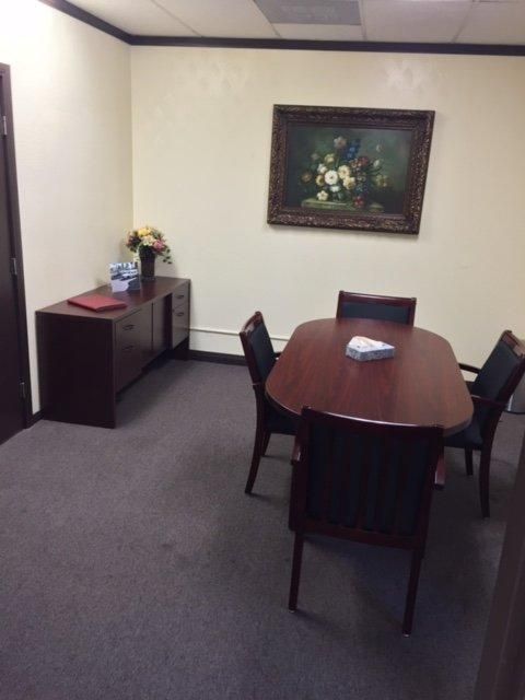 Small office conference room with oval table, chairs, side cabinet, and framed painting on the wall.