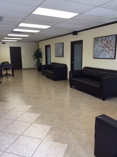 Office lobby with black couches, tiled floor, framed art, and fluorescent ceiling lights