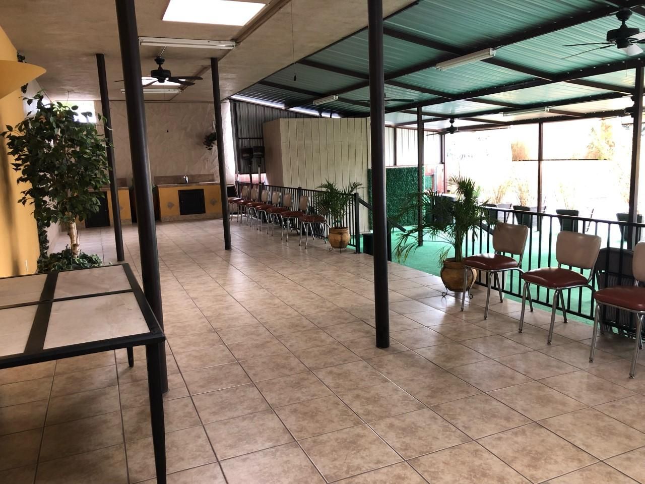 Covered outdoor patio with tables and chairs under a metal canopy, tiled floor, and potted plants.