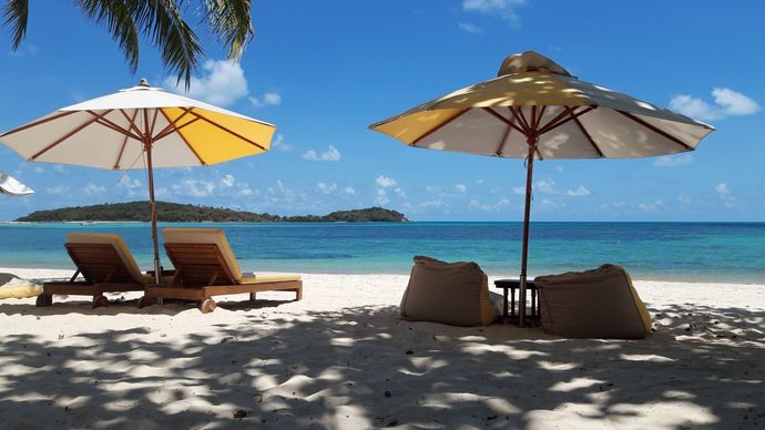 Ligstoelen en zitzakken staan ​​onder twee parasols op een zonnig tropisch strand met uitzicht op de oceaan.