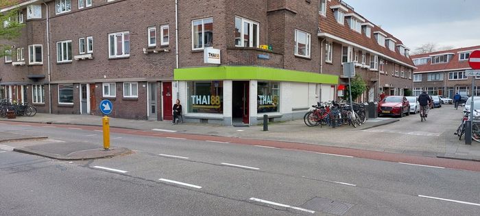 Een straathoek met een bakstenen appartementencomplex en een klein winkeltje met een felgroen uithangbord.