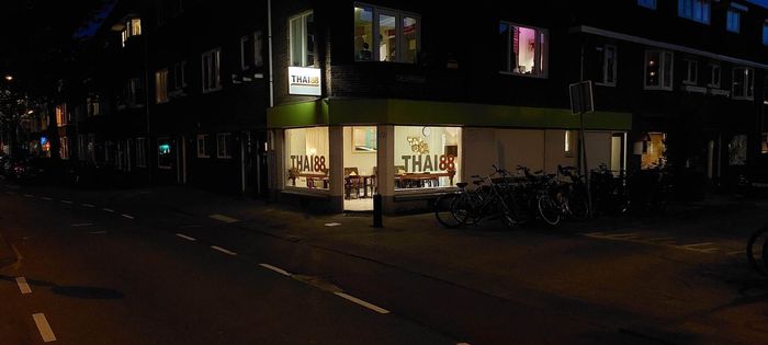 Op een straathoek 's nachts is een felverlichte winkel te zien met een groene luifel en fietsen die buiten geparkeerd staan.