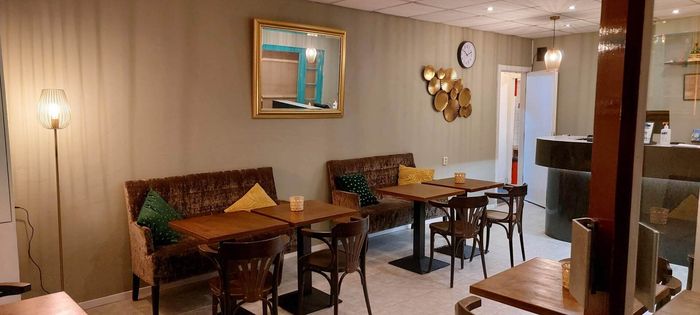 Interieurfoto van een eetgedeelte met twee tafels, bruine fluwelen zitbanken, decoratieve spiegels en warme verlichting.