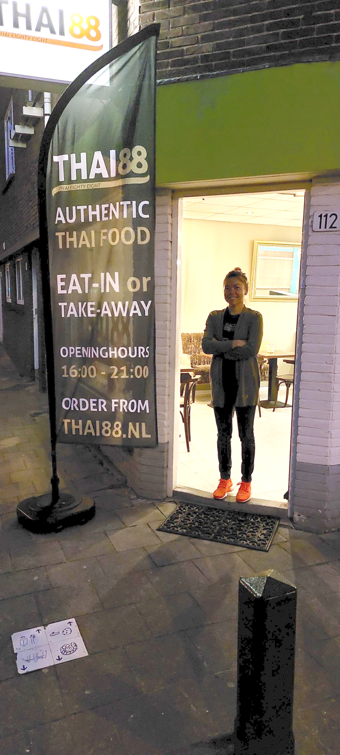 Een persoon staat in de deuropening van een Thai88-restaurant naast een uithangbord met reclame voor authentiek Thais eten.