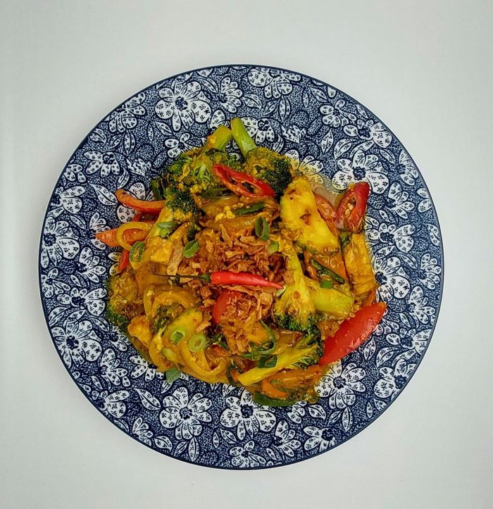 Roerbakgerecht met broccoli, rode pepers en gebakken uien op een blauw-wit bord met bloemenpatroon.