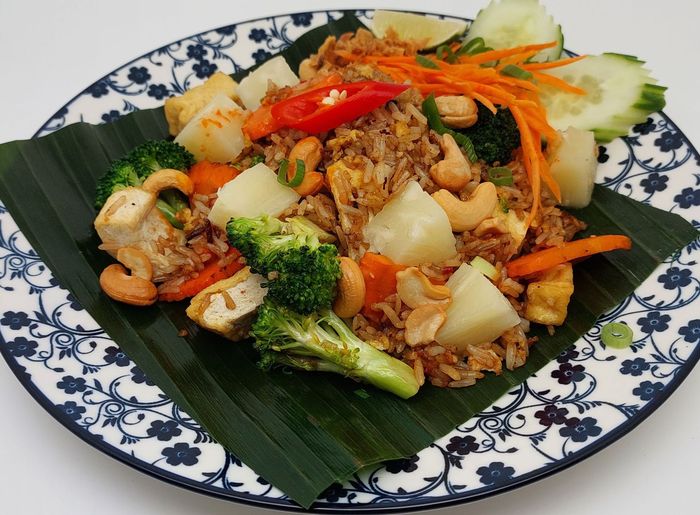 Een bord ananas-gebakken rijst met tofu, broccoli, cashewnoten en geraspte wortel, geserveerd op een bananenblad.