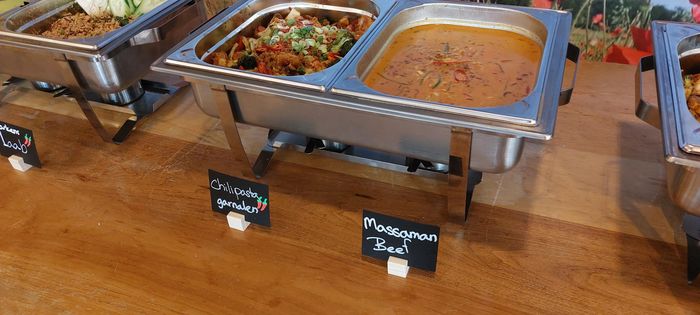 Een buffetlijn met metalen warmhoudschalen gevuld met diverse etenswaren op een bruine toonbank.