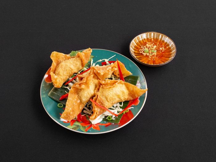 Een bord met knapperige, goudbruine gefrituurde wontons, gegarneerd met kruiden en rode pepers, geserveerd met een dipsausje.