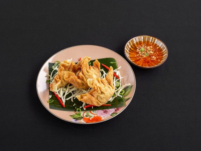 Gefrituurde dumplings op een bord bekleed met geraspte kool en bananenbladeren, geserveerd met een klein schaaltje chilisaus.