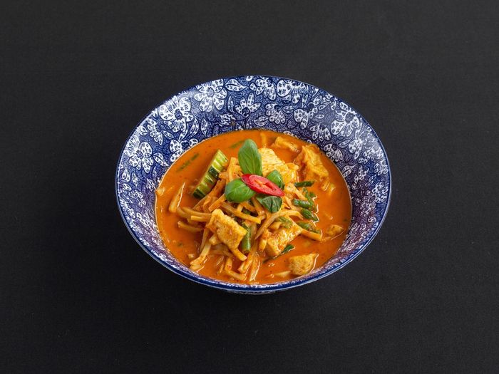 Een kom pittige rode curry met tofu, bamboescheuten en sperziebonen, gegarneerd met basilicum en een schijfje rode chilipeper.