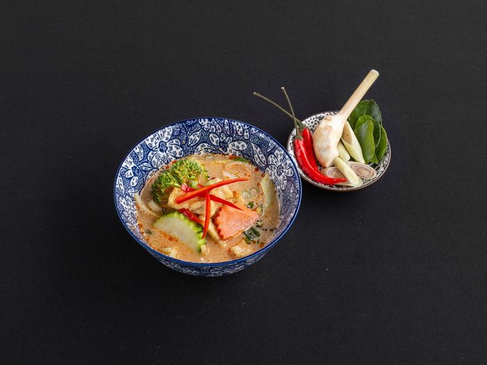 Een kom romige Thaise curry met groenten, naast een klein schaaltje met chilipeper, citroengras en kaffirlimoenblaadjes.