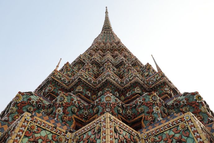 Een opname vanuit een laag perspectief van een hoge, gelaagde Thaise stoepa, versierd met ingewikkelde, kleurrijke keramische tegels met bloemmotieven, tegen een lichte hemel.