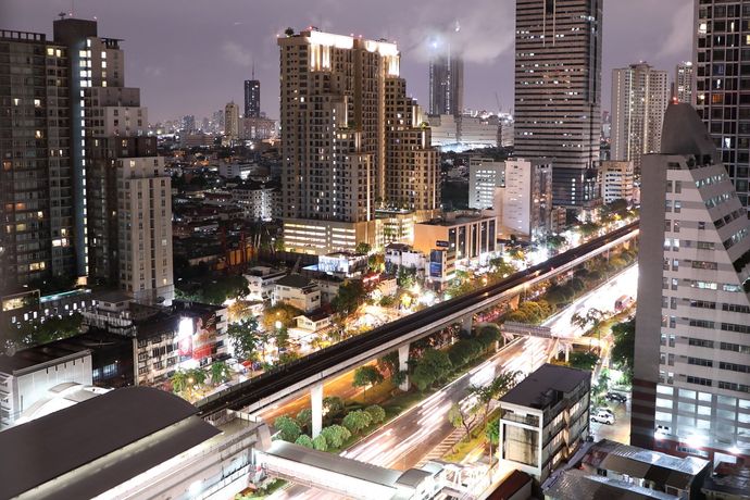 Een nachtelijk uitzicht op een felverlichte stadsskyline met een verhoogd treinspoor dat boven drukke, door verkeer gevulde straten loopt.
