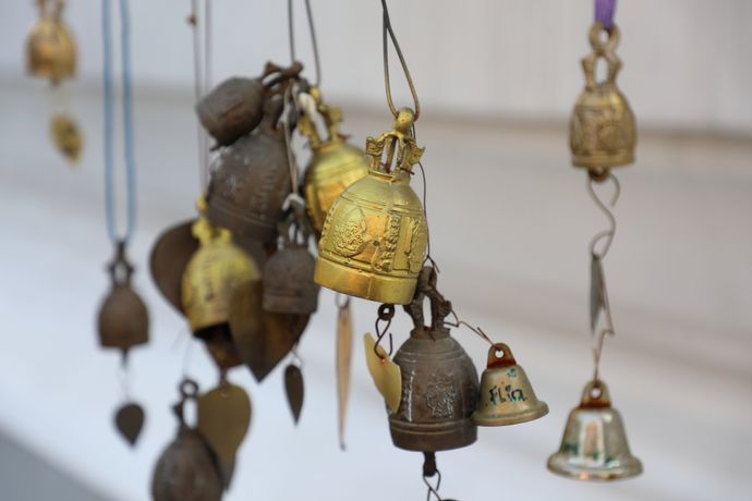 Een groepje verschillende hangende metalen gebedsbellen, sommige goudkleurig en andere verweerd, tegen een wazige witte achtergrond.