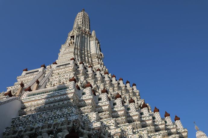 De sierlijke, witte, gelaagde torenspits van de Wat Arun-tempel steekt af tegen een heldere, diepblauwe hemel.