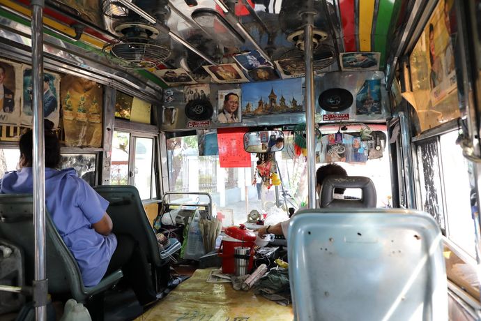 Het interieur van een versierde bus met kleurrijke posters, luidsprekers en passagiers die in stoelen zitten die naar voren gericht zijn.