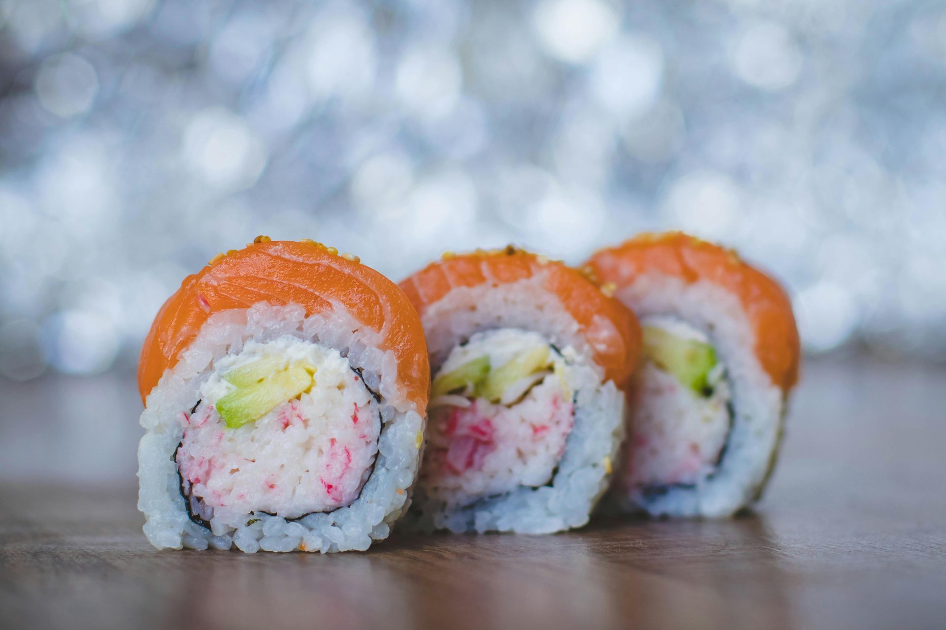 Three sushi rolls are sitting on a wooden table.