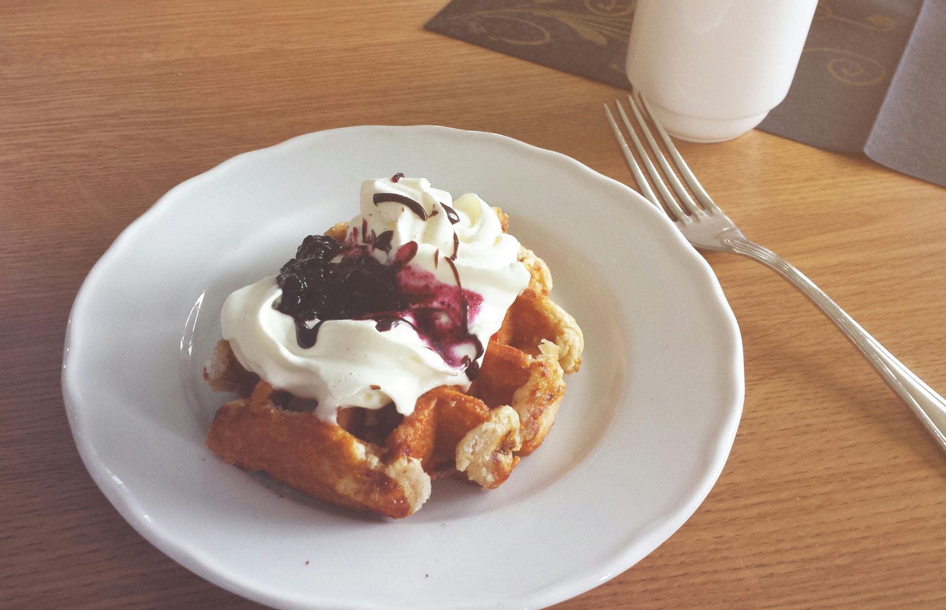 A waffle with whipped cream and blueberry sauce on a white plate