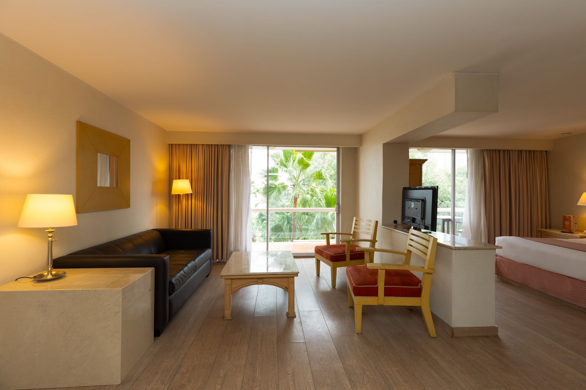 Habitación de hotel moderna con sofá, dos sillas, cama y puerta de balcón con cortinas.