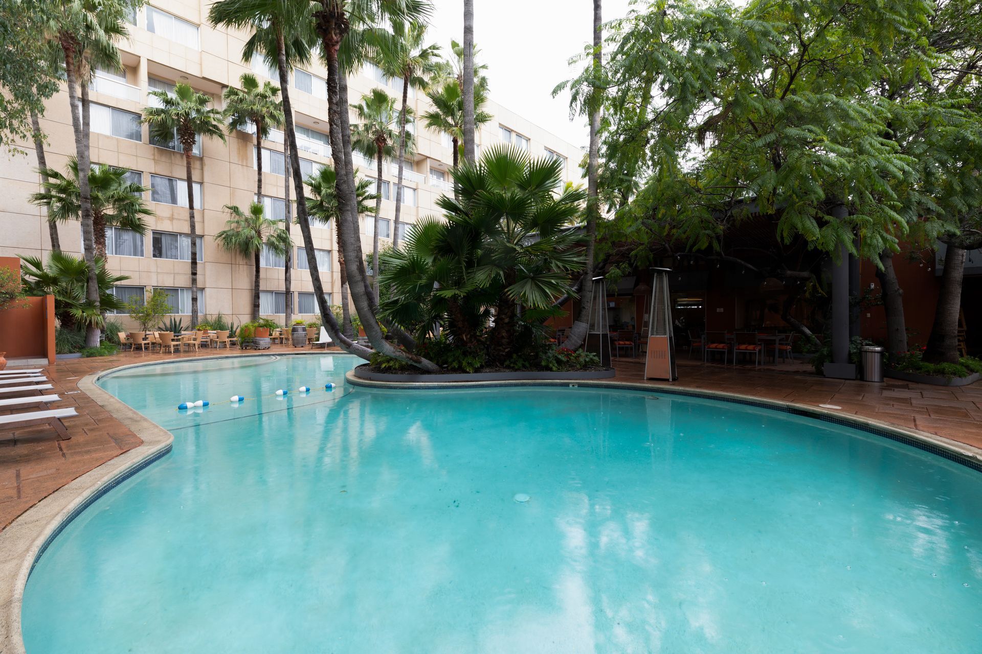 Piscina turquesa del complejo junto a palmeras y un edificio de hotel.