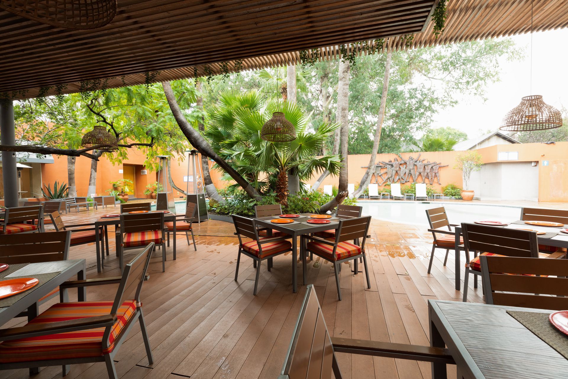Terraza de restaurante al aire libre con mesas y sillas de madera bajo un techo que proporciona sombra, rodeada de vegetación.