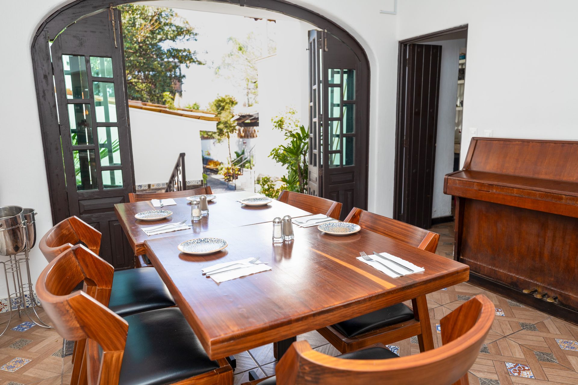 Comedor con mesa de madera, sillas y juego de té frente a una luminosa ventana arqueada.