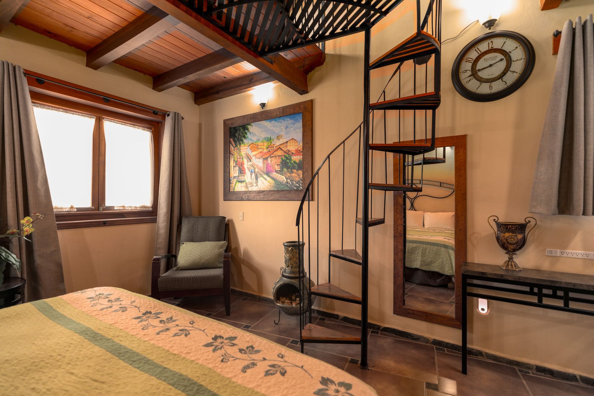 Acogedora habitación tipo loft con vigas de madera, escalera de caracol, silla, alfombra, ventana y reloj de pared.