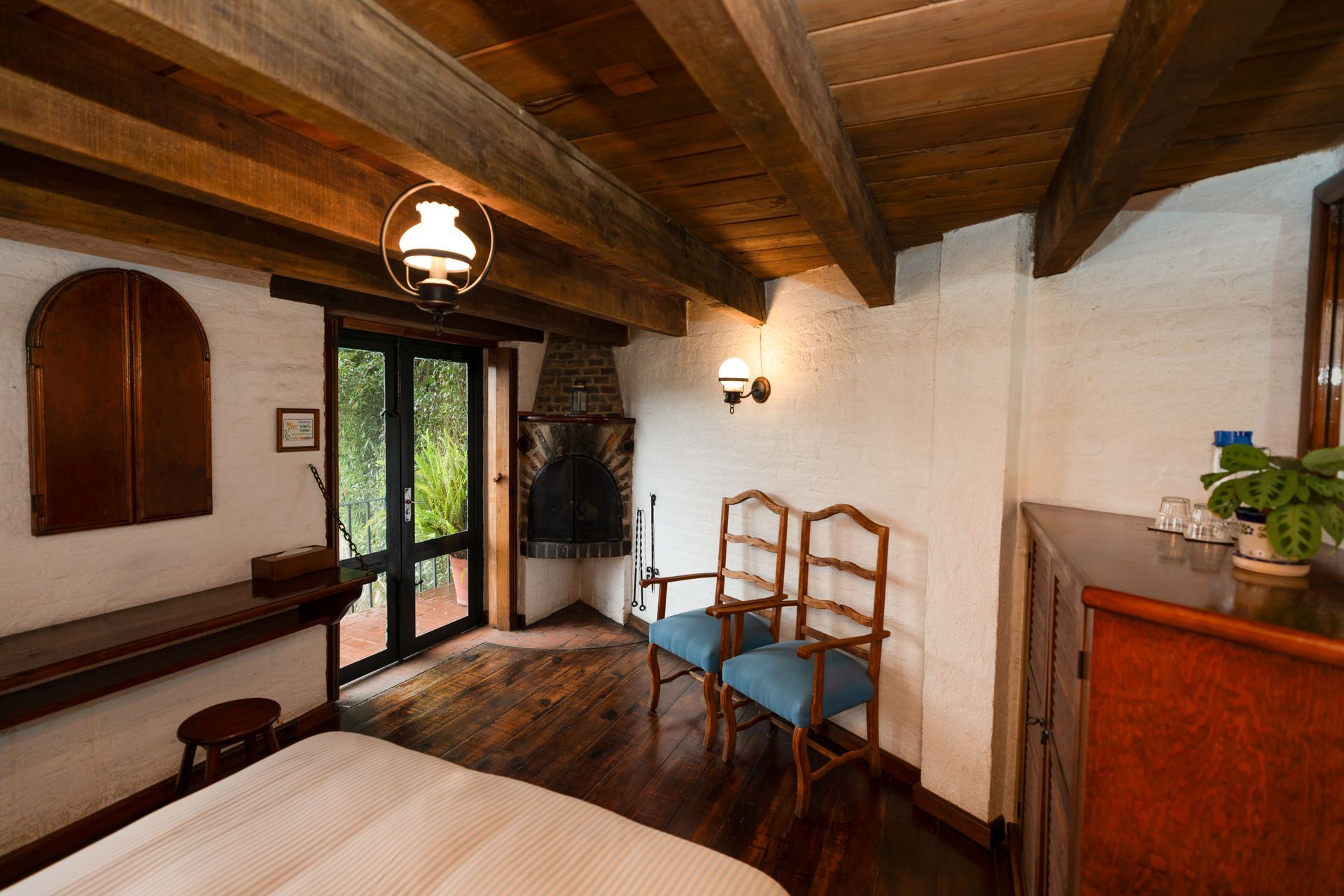 Acogedor dormitorio rústico con vigas de madera, cama, sillas y puertas francesas que dan al exterior.