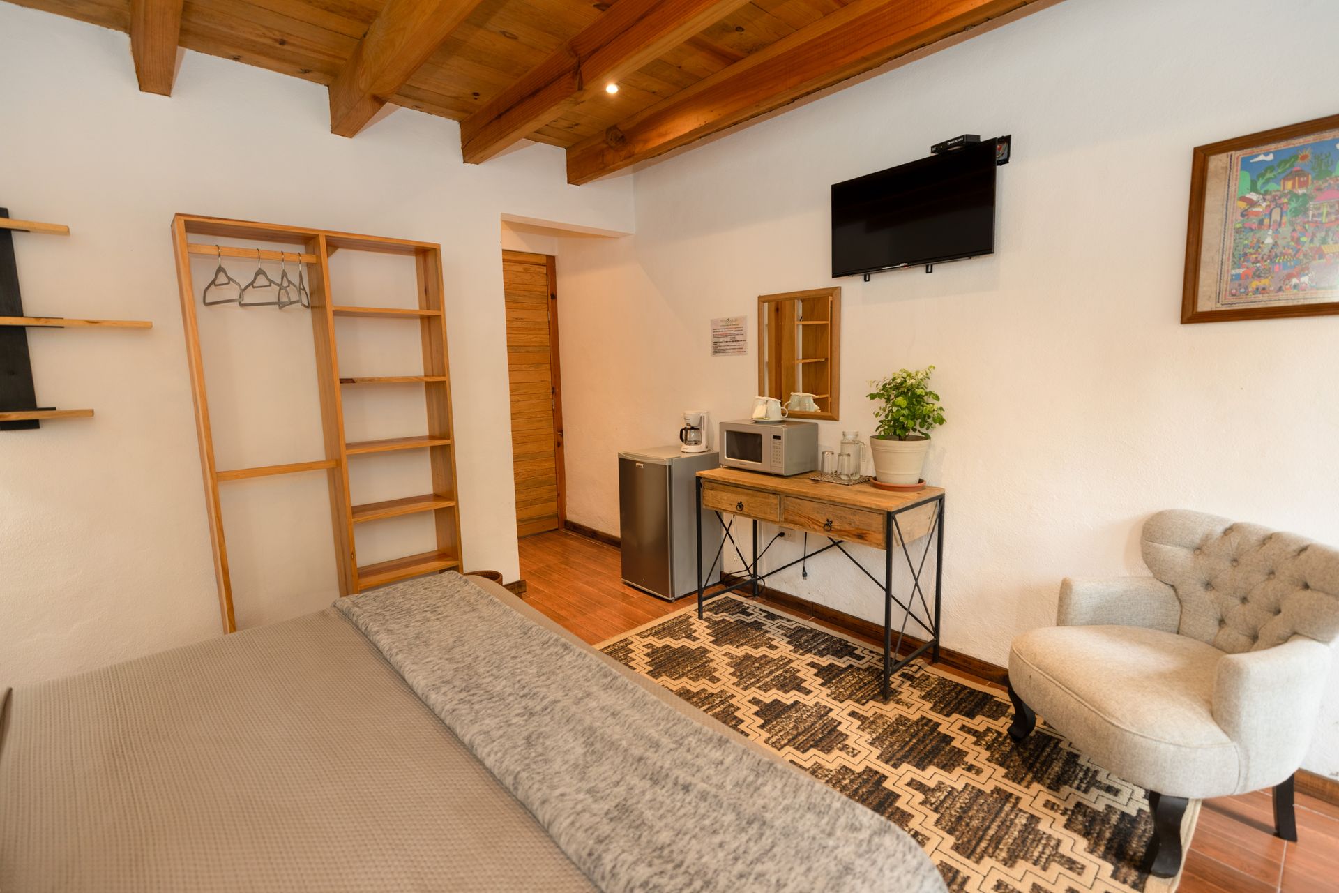 Dormitorio moderno con techo de madera, cama, escritorio, televisor de pared y alfombra estampada.