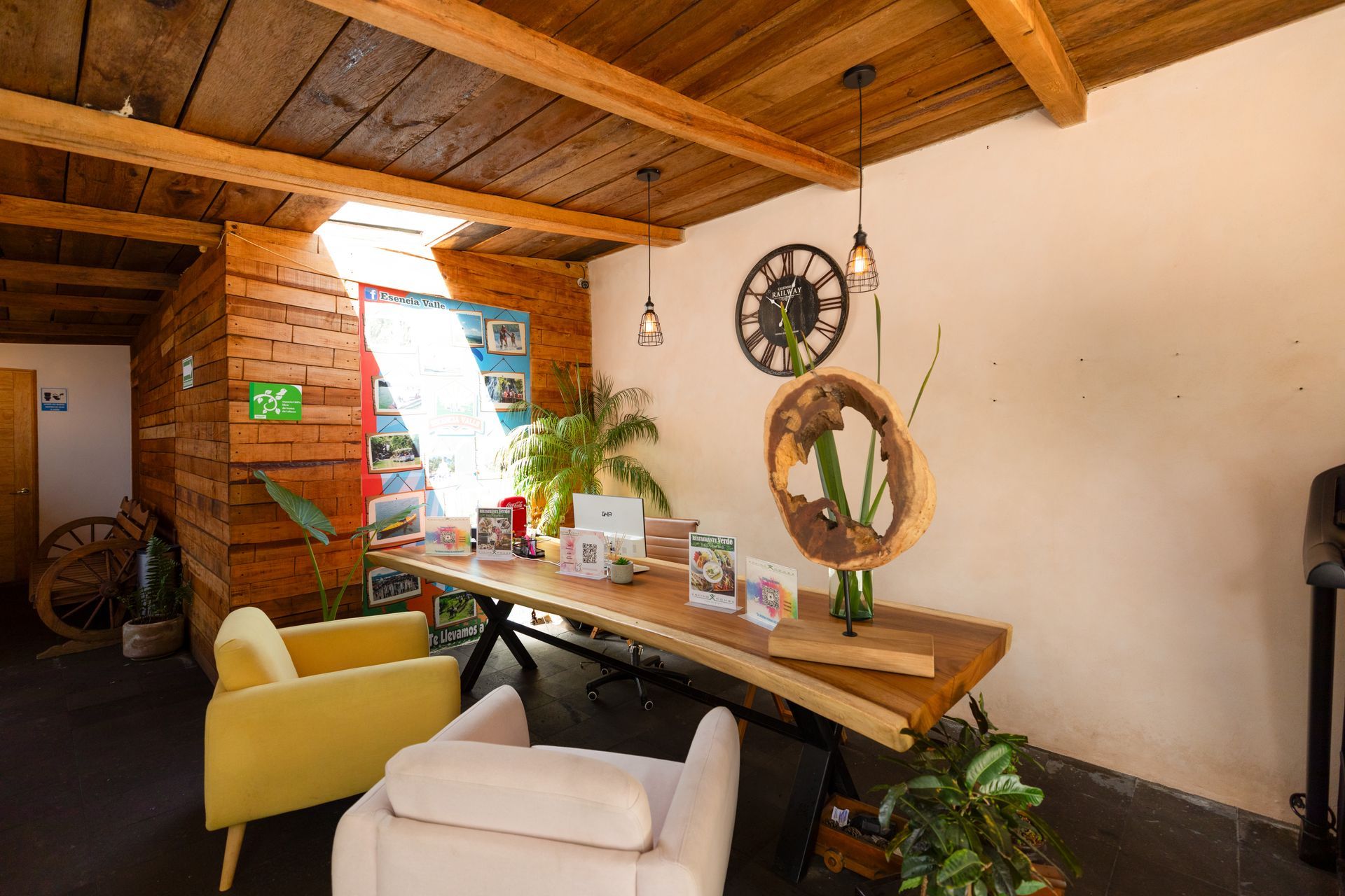 Acogedora sala de estar rústica con techo de madera, mesa larga, sillas, plantas y decoración de pared.