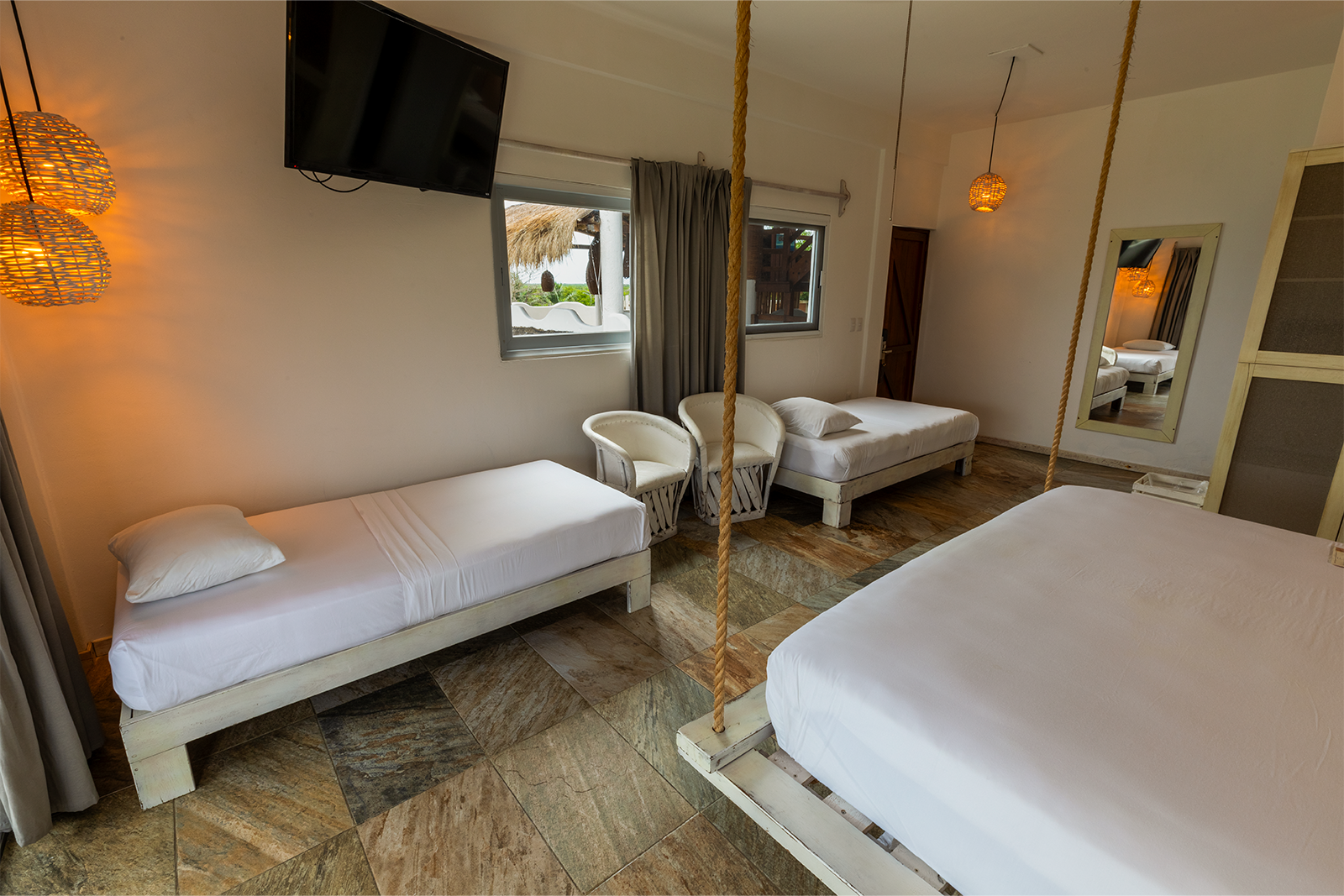 Habitación luminosa con tres camas individuales, puertas de armario con espejos y lámparas colgantes cálidas.