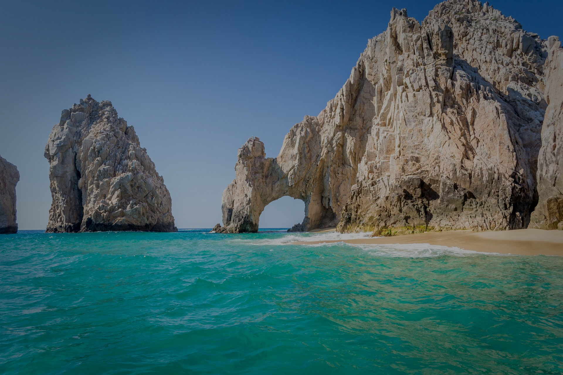 Mar turquesa con acantilados rocosos y un arco natural bajo un cielo azul claro.