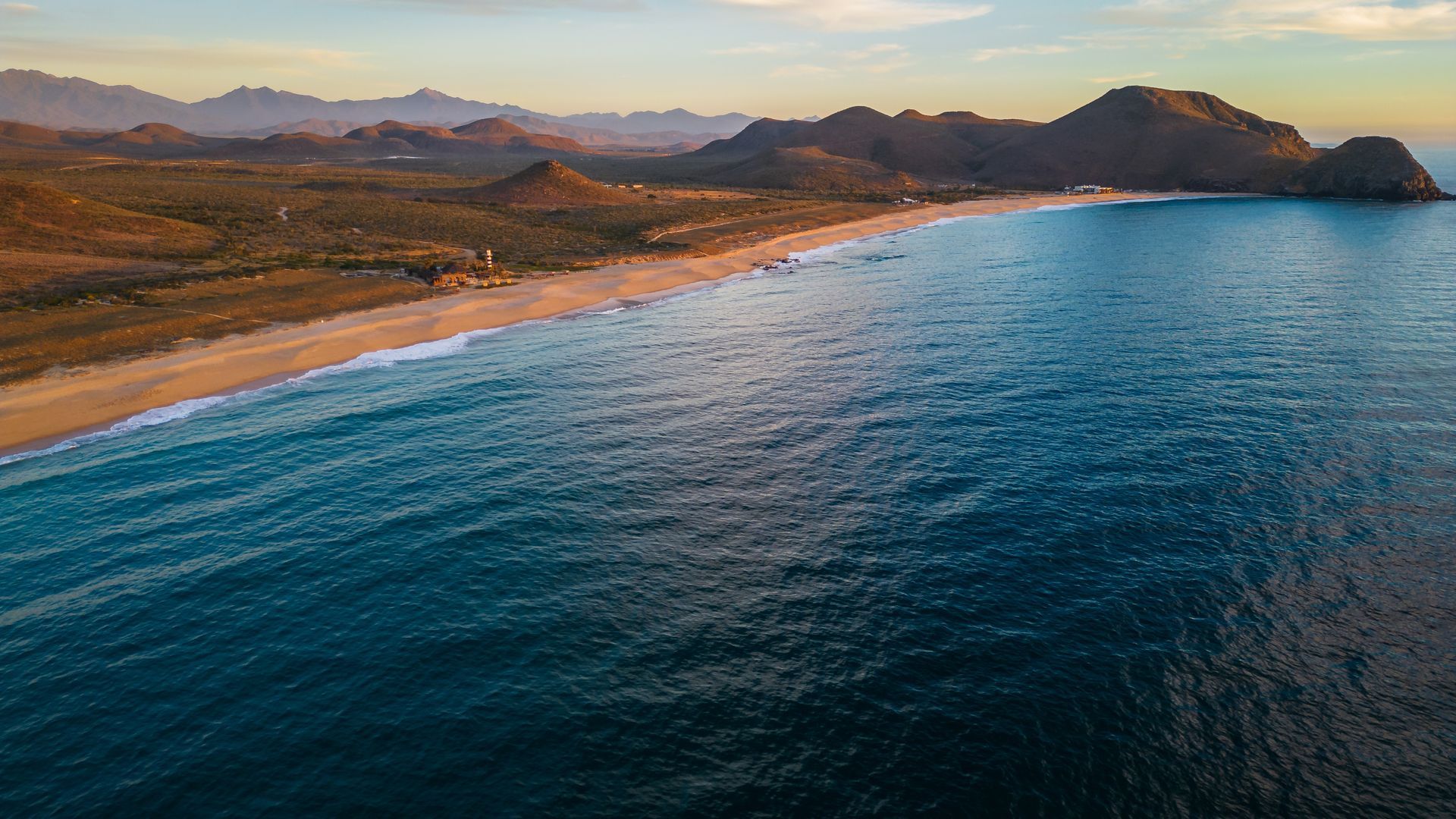 Vista aérea de una playa abarrotada con coloridas sombrillas, la orilla y agua verde cerca.