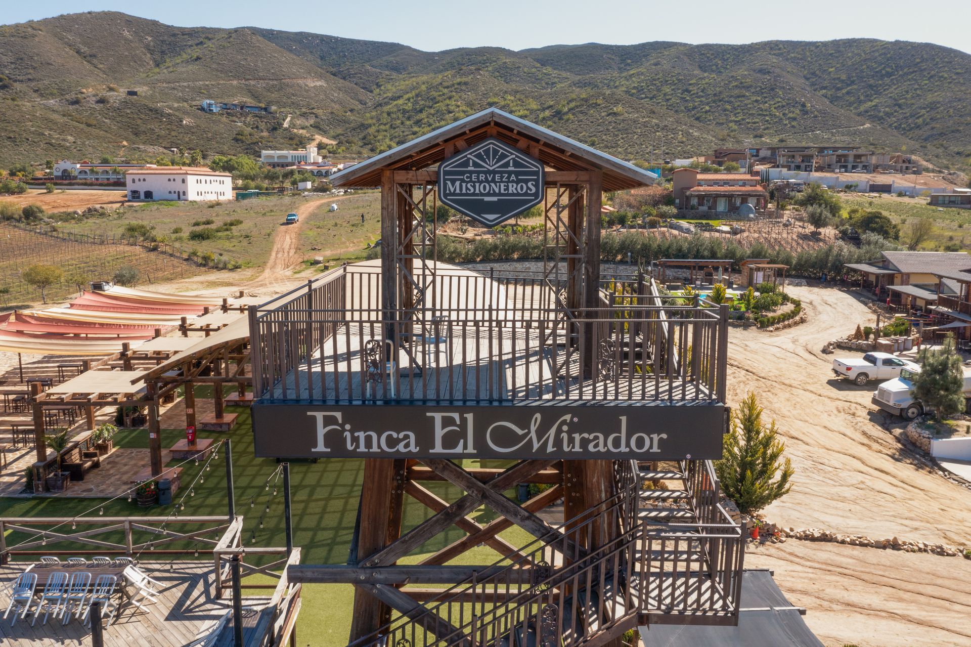 Entrada a la Finca El Mirador con letrero de madera, asientos en el patio y colinas al fondo.