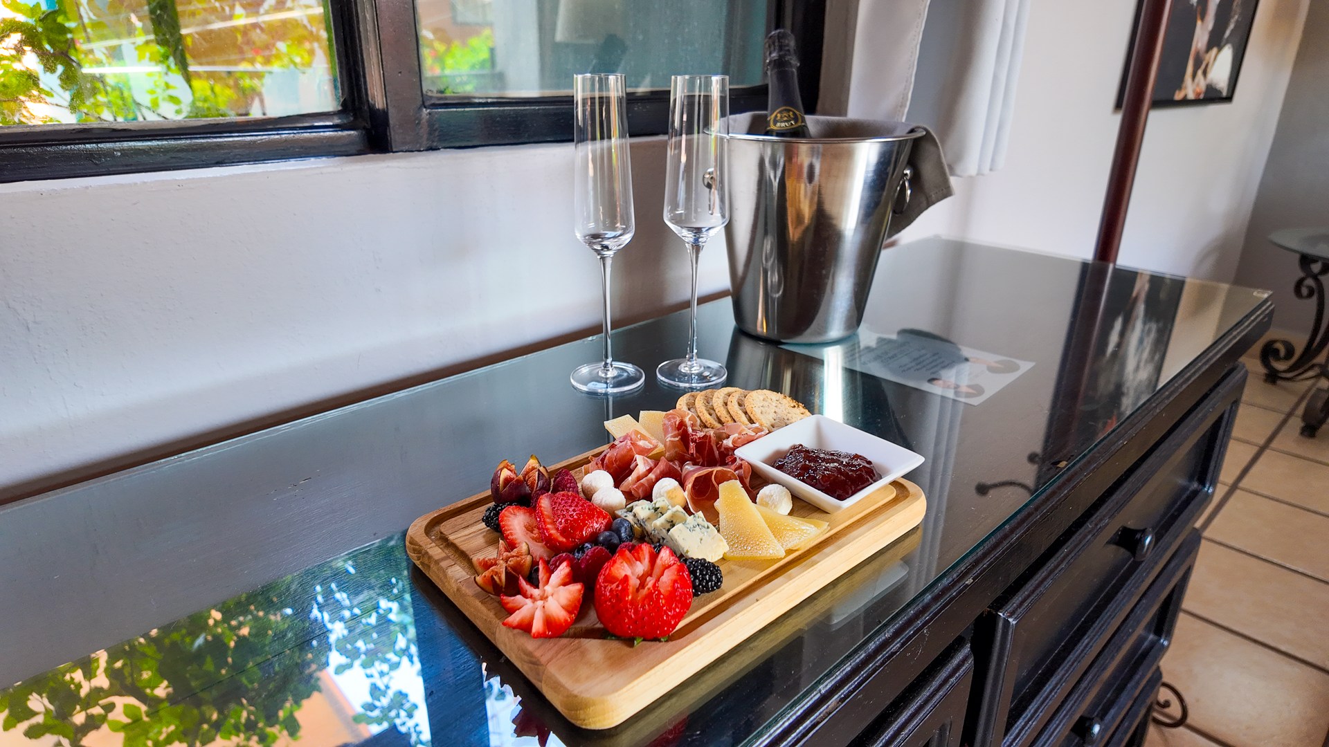 Plato de frutas con fresas, arándanos y queso sobre una mesa de cristal junto a una ventana.
