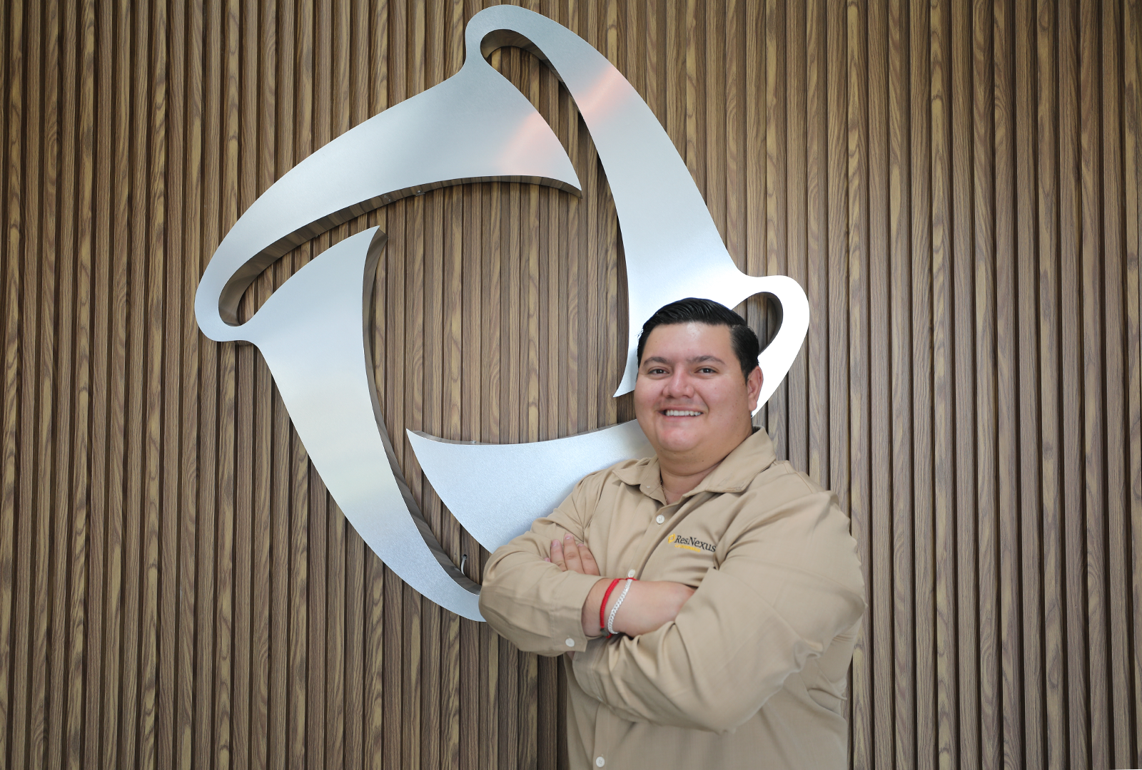 Retrato de un hombre con camisa blanca y el logotipo de ResNexus, de pie frente a un fondo de oficina borroso.
