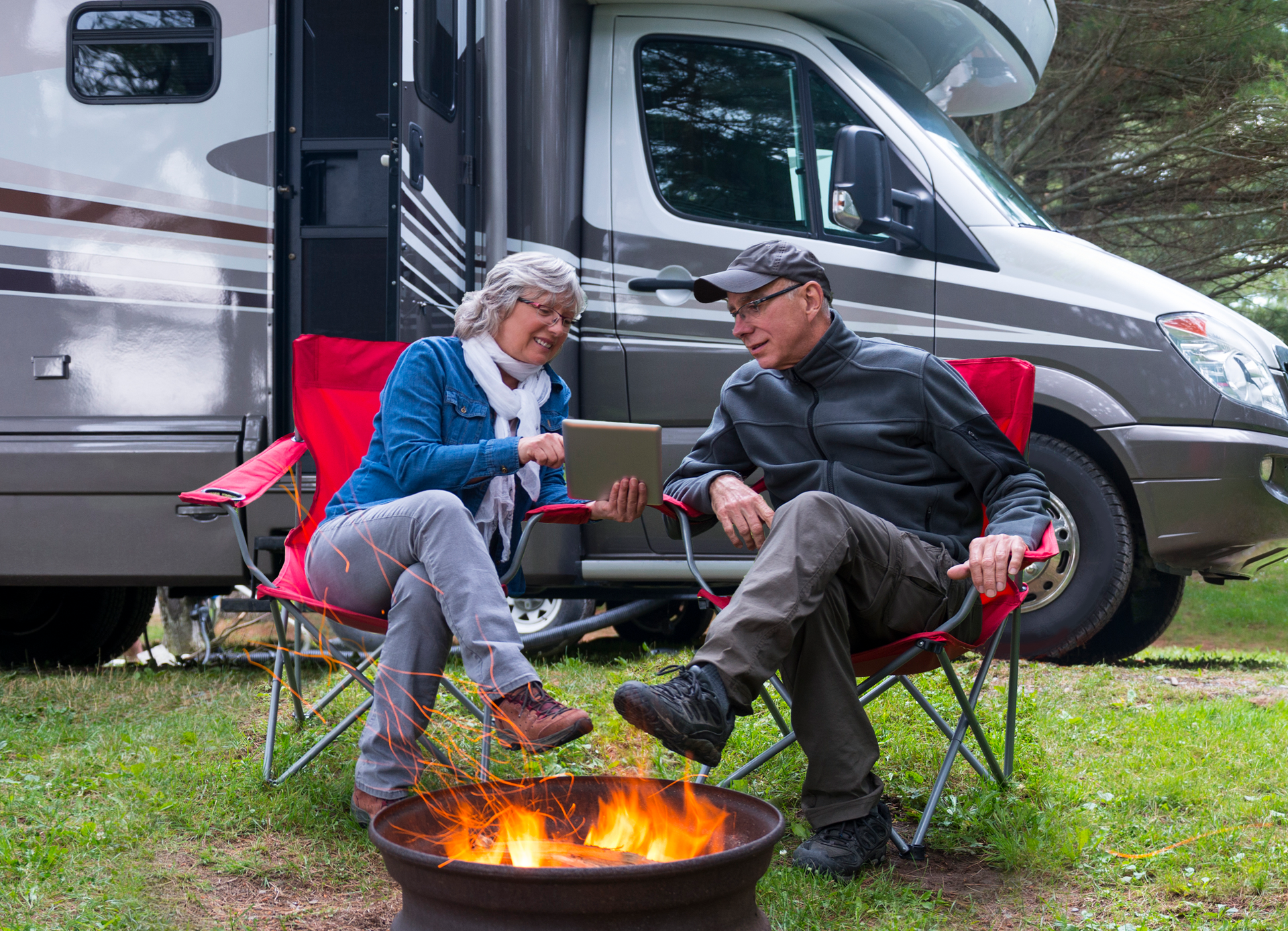 elderly couple looking at a laptop, nearby a campfire and an RV