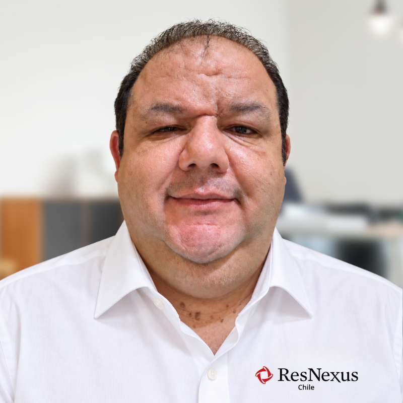Retrato de un hombre con camisa blanca y el logotipo de ResNexus, de pie frente a un fondo de oficina borroso.